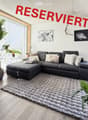 Modern living room with a grey sectional sofa, large shaggy rug, potted plants, and artwork on the walls.
