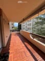 Wooden deck balcony with glass railing, beige awning, and view of neighboring buildings and greenery.