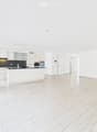 Bright, open-plan living and kitchen area with white tiled flooring, white kitchen cabinets, a central island, and modern appliances.