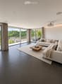 Modern living room with large windows offering a scenic view, featuring a white sectional sofa, wooden coffee table, and projector mounted on the wall.