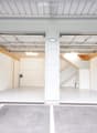 Modern, spacious garage with two large open doors, clean white interior, and a concrete parking area outside.
