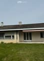 Single-story house with beige siding, dark tiled roof, multiple windows, and a covered entrance with a pink awning.