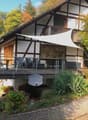 Traditional half-timbered house with a spacious wooden balcony, outdoor furniture, and surrounding garden area.