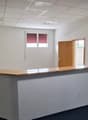 Empty office space with a reception desk, white walls, carpeted floor, and multiple doors leading to other rooms.
