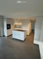 Modern kitchen with white cabinets, a central island, built-in oven, and a sink. The space features large windows and a view of the outdoor area.