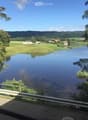 Garden / Outdoor Area. A serene view of a river surrounded by lush green trees and fields, with a few houses visible in the distance under a clear blue sky.