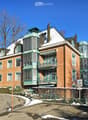 A multi-story brick building with green balconies and a snow-covered roof, situated on a hillside with a curved road in front.