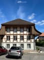 Two-story traditional half-timbered house with white plaster walls and wooden beams, multiple windows, and a tiled roof. Two cars are parked in front.