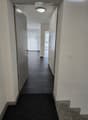 Clean, modern hallway with dark tiled floor, white walls, and a ceiling light. Features a partially open door leading to another room and a staircase with granite steps.