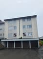 Four-story apartment building with multiple windows and a row of garages at the bottom.
