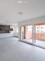 Modern, unfurnished living space with a fully equipped kitchen area, large sliding glass doors leading to a balcony, and grey tiled flooring.