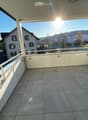 Balcony with tiled floor, white railings, and a view of a residential area with houses and greenery.