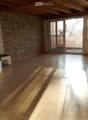 Empty room with wooden floor, exposed wooden ceiling beams, stone accent wall, large windows, and sliding glass doors leading to a balcony.