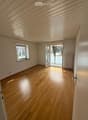 Empty room with wooden flooring, white walls, large window, and sliding glass door leading to a balcony.