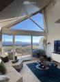 Bright living room with large windows and a view, featuring a sofa, coffee table, and television.