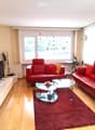 Modern living room with red leather sofas, a glass coffee table, a TV stand, a glass cabinet, and a plant near the window.