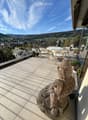 A balcony with a table and chairs, a statue, and a view of the mountains and town