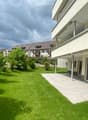 Well-maintained garden with green lawn, trimmed bushes, and a modern house with large windows and a balcony.