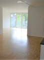 Empty room with wooden flooring, white walls, and a small kitchen area with a sink and cabinets. Large sliding glass doors lead to a balcony.