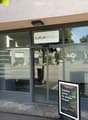 The image shows the exterior of a modern building with large glass windows and a sign reading "AURUM HEALTH & PERFORMANCE". A promotional sign in front advertises a training program. The building has a clean, contemporary design with a visible entrance an