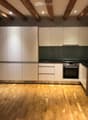Modern kitchen with white cabinets, stainless steel oven, and wooden flooring.