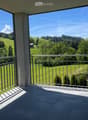 Balcony with metal railing, tiled floor, overlooking green hills and trees under a clear blue sky.