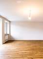 Empty room with wooden flooring, white walls, and large windows allowing natural light. No furniture or equipment is present.