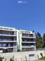 Modern multi-story apartment building with balconies, green facade, and a raised ground floor with a garage entrance.