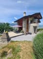 Two-story house with stone and wood exterior, balcony, outdoor dining area, and scenic mountain view.