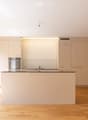 Modern kitchen with light-colored cabinets, a central island, and a built-in oven. The space features wooden flooring and large windows allowing natural light to fill the room.
