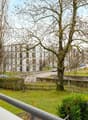 Balcony overlooking a landscaped garden area with trees, modern apartment buildings, and a road with parked cars.