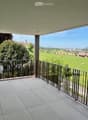 Spacious balcony with tiled floor, metal railing, and scenic view of a green field and town.