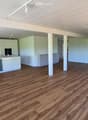 Open-plan space with light-colored wooden flooring, white cabinetry, and a staircase leading to an upper level. The area is unfurnished and appears to be a combined living and kitchen area.