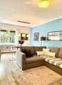 Modern living room with a grey sectional sofa, coffee table, dining table, chairs, and decorative items including a flower vase and picture frames.