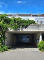 Modern concrete building with a covered entrance, greenery on the roof, and a spacious driveway.