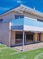 Modern two-story house with light-colored facade, large windows, and a spacious balcony overlooking the front yard.