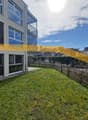 Well-maintained lawn with wooden fence, small tree, and modern house with large windows and balcony in the background.