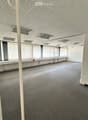 Empty room with grey carpet, white walls, large windows with blinds, and a perforated white ceiling with recessed lighting.