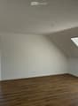 Completely empty room with wooden flooring, white walls, and large windows, including a skylight. No furniture or equipment.