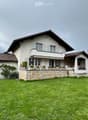 Two-story house with a stone base, white upper facade, multiple windows, and a well-maintained lawn.