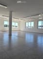 Empty room with tiled floor, white walls, large windows, and a central column. No furniture or equipment present.