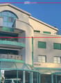 Modern multi-story building with curved facade, green shutters, balconies, and a Nissan dealership entrance.