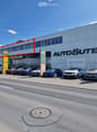 Modern car dealership building with large glass windows and signage for 'AUTOSUTER', several cars parked in front.
