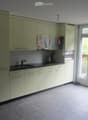 Kitchen. Modern kitchen with light-colored cabinets, a sink, an oven, and a window with a curtain. The floor is tiled, and there are some shoes near the window.