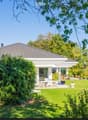 A white house with a tiled roof is surrounded by a well-maintained garden, featuring a patio area with outdoor furniture and a scenic view of the countryside.