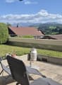 Balcony with a view of mountains, featuring two chairs, a small table, and a milk can as a decorative element.
