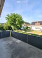 Balcony with metal railing overlooking a residential area with houses, trees, and a clear sky.