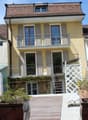 Two-story residential building with a balcony, wooden deck, and stairs leading to the entrance.