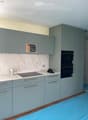 Modern kitchen with light blue cabinets, marble backsplash, induction stove, and double oven. Countertop has a few items including a bottle and a hat.