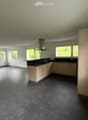 Empty kitchen with light wooden cabinets, black countertops, and large windows overlooking a green landscape.